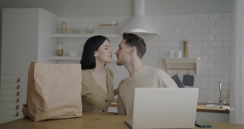 Couple with Groceries at Kitchen Table with Laptop