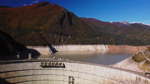Hoher Betonbogendamm mit Fluss inmitten grüner Berge, mit Drohne gefilmt