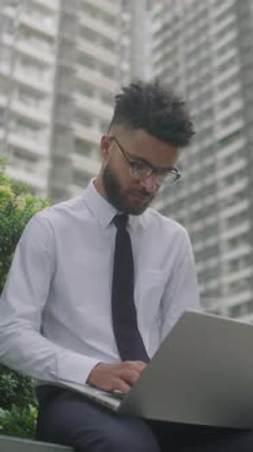 Professional Man Typing on Laptop in Urban Setting