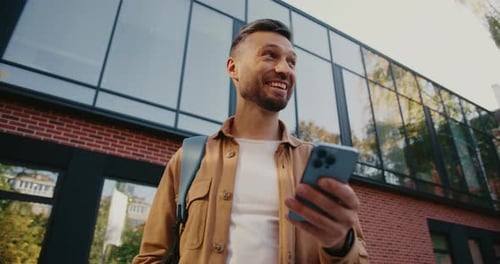Bottom View on Happy Caucasian Man Using Cell Phone While Standing in Middle of Street Chatting on