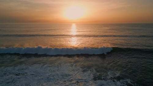 Golden sunrise on serene ocean surf washing coastal beach drone view