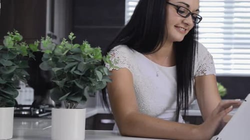 Brunette woman uses tablet computer for retail internet shopping in her kitchen