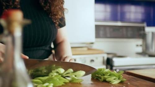 Cook Chopping Celery on Cutting Board Surrounded by a Variety of Ingredients