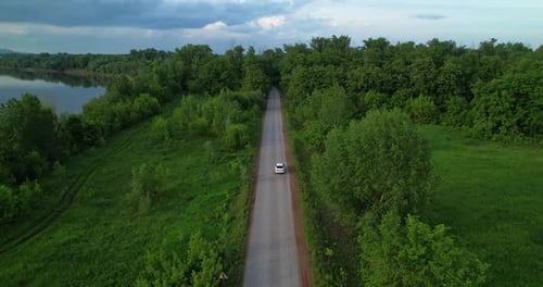 A White Car is Driving Along the Road Going Into the Forest