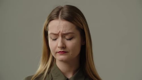 A Young Woman Stands in Front of the Camera and Frowns Upset Blonde Woman Stands on a Gray
