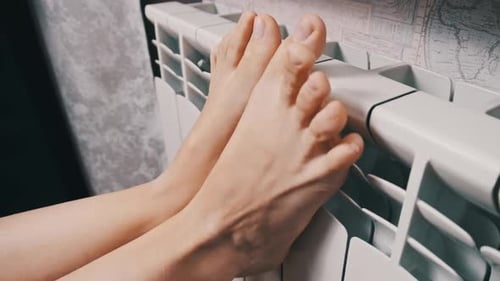 Female Bare Feet Touch the Heating Radiator Trying to Keep Warm