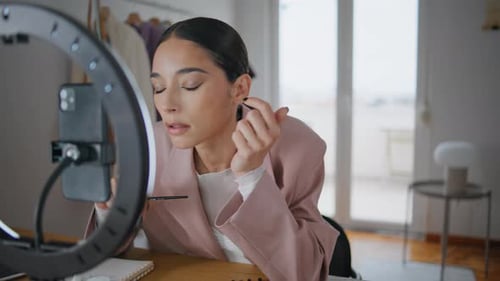 Influencer haciendo una reseña de maquillaje para la cámara de un teléfono inteligente en Room Closeup. Mujer visagista
