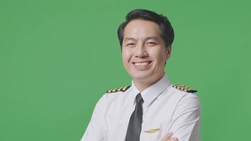 Nahaufnahme einer Seitenansicht eines asiatischen Piloten, der lächelt und seine Arme im Greenscreen-Hintergrund verschränkt