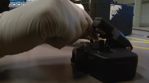 Hände legen Glasfaserkabel in ein hochpräzises Schneidgerät im photonischen Labor. Glasfaser-Schneidwerkzeug