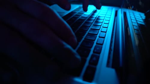 ein männlicher Programmierer, der Code auf einer Tastatur schreibt. Blaue Beleuchtung, Nahaufnahme