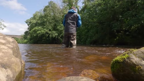 Low angle shot of a fisherman wading and fly fishing in murky brown water