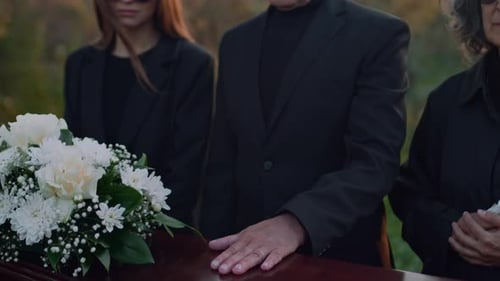 Mourners Gather around Coffin with Bouquet of Flowers