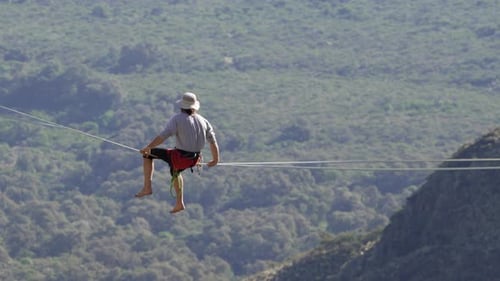 A man contemplates the forest below while sitting on a highline. Beauty in nature, extreme sport, 4k