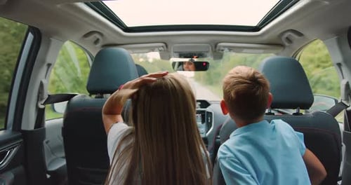 Positive Two Teen Kids Watching at the Road from Car Backseat During Trip Together with Mother