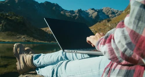 Woman on Trip Using Laptop Computer Sitting on Mountain Lakeshore and Typing