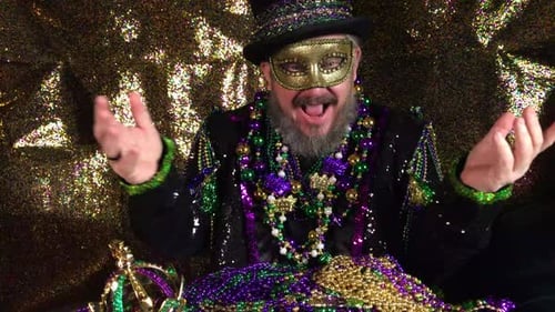 Happy Mardi Gras man in fancy costume with top hat holding pile of beads
