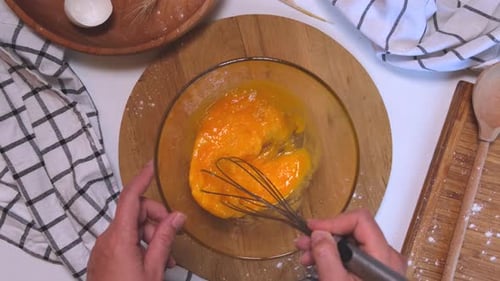 Weibliche Hände, die Eier mit einem Schneebesen oder Eigelb mit Zucker verquirlen, um Pfannkuchen oder Pfannkuchen zuzubereiten