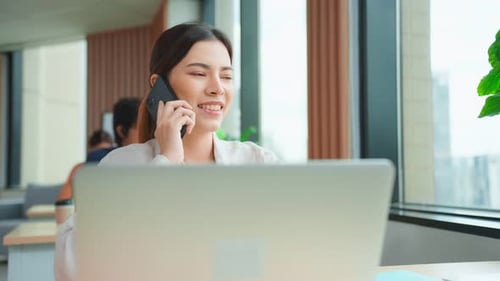 Asian happy businesswoman talking on smartphone and working in office.
