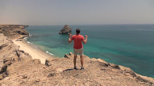 Young Man Raising Arms in Victory Standing on Cliff Near Ocean, Super