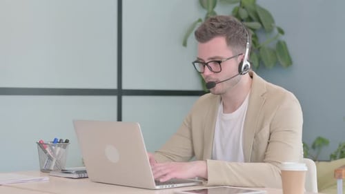 Young Businessman with Headset Talking with Customers Online in Call Center