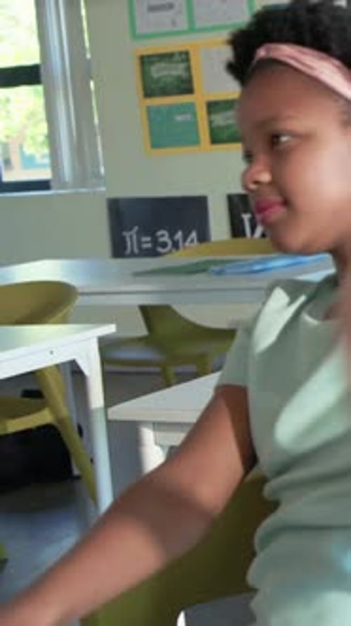 Vertical video: Reacting to cue, girl in green shirt raising arms at desk, pi poster, copy space