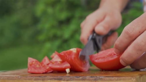 Side view of male hands cutting fresh red tomato on board to prepare salad