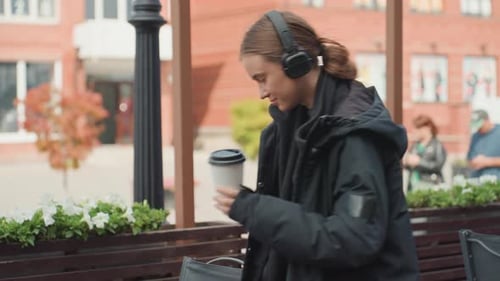 Woman Sits at Cafe Listening to Music Drinking Coffee