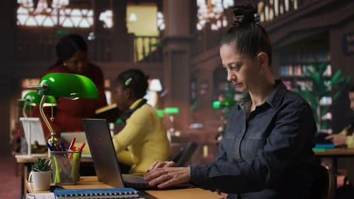 Porträt einer selbstbewussten Bibliothekarin, die in einer öffentlichen Bibliothek an ihrem Laptop arbeitet