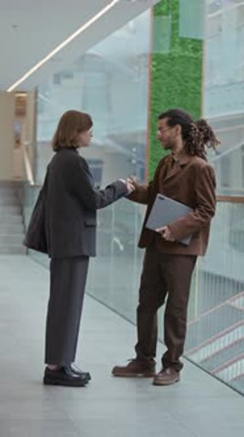 Young Diverse Business Couple Shaking Hands near Glass Wall in Office Building