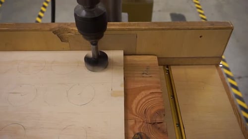Close-up clip of a drill press in the process of drilling a hole in a small sheet of plywood. Locate