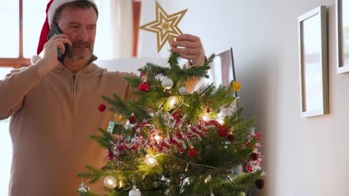 Man Decorating Christmas Tree While Talking on Phone