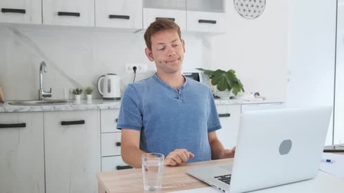 Man Stretching While Working at Laptop in Kitchen