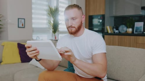 Close Up Face Handsome Man Using Tablet Computer Focused Sitting on Sofa at Home Online Technology