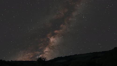 Nachts erhebt sich die Milchstraße über den Hügeln auf dem Land mit Sternen und einem schwarzen Loch im galaktischen Zentrum 4K