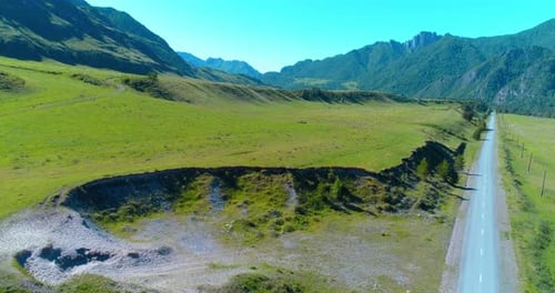 Route de montagne rurale aérienne et prairie au soleil d'été, route asphaltée et rivière