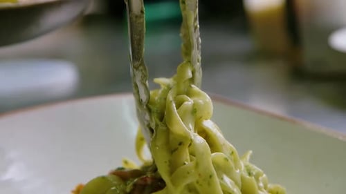 Tongs Placing Fettuccine Alfredo into Dish