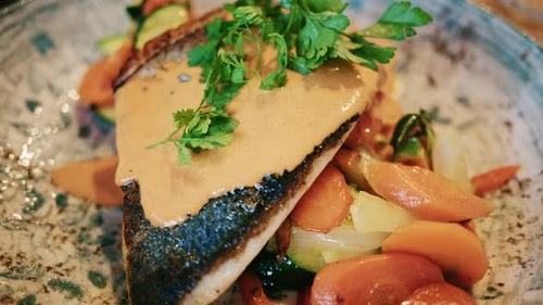 Close up of a plated fish fillet served with vegetables and creamy sauce in a restaurant setting