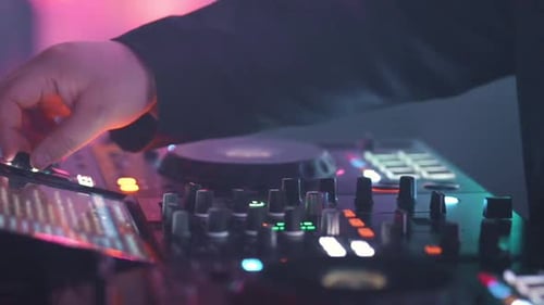 Gros plan : DJ Hands mixant de la musique sur une manette et un fader lors d'une soirée électronique avec des lumières de boîte de nuit