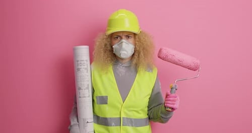 Serious Attentive Responsible Female Builder Wears Hardhat Uniform and Protective Respirator Holds