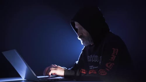 Hooded Figure Typing on a Laptop in the Dark