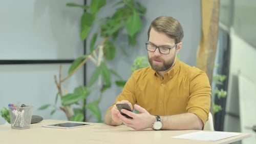 Excited Man Celebrates Success on Phone at Desk
