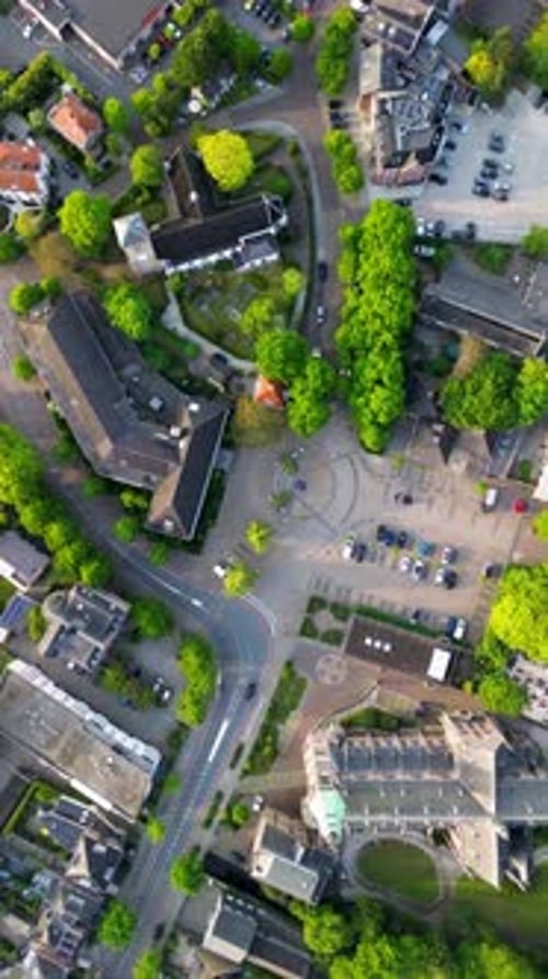Aerial view of a town block with a central plaza multi-story buildings a church and tree-lined roads