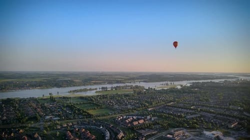 Colorful hot air balloon flying over buildings in small european city in 4k at summer sunset, aerial