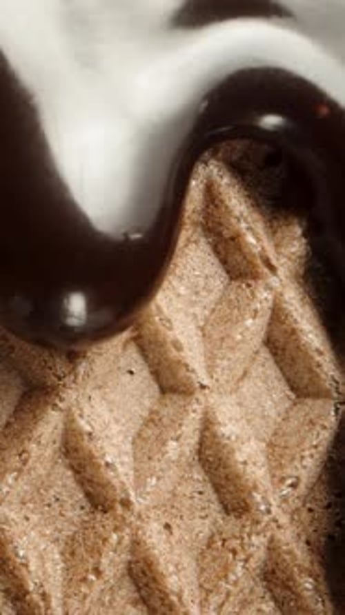 Vertical video. Dark chocolate is flowing down a waffle, creating a textured pattern. Macro slider.