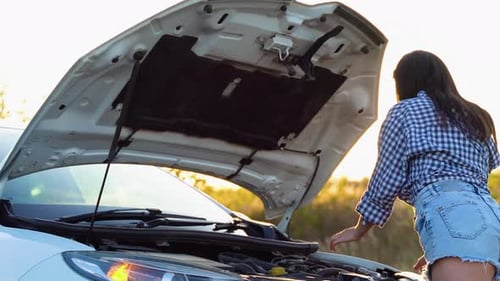 Beautiful Woman in Shirt and Shorts Looks in Open Car Hood on a Road