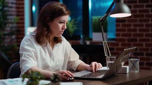 Trabajador escribiendo en el teclado y escribiendo documentos comerciales financieros en una computadora portátil