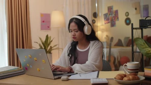Young Adult Uses Laptop with Headphones at Desk