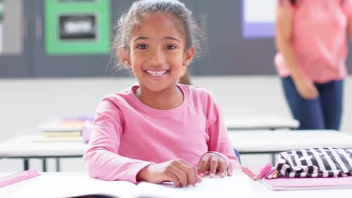 Smiling girl sitting at desk in school classroom with open notebook