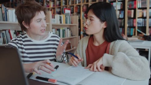 Female College Friends Discussing Homework on Laptop in Library