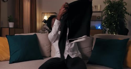 Young Man Examines Shirt on Couch at Night